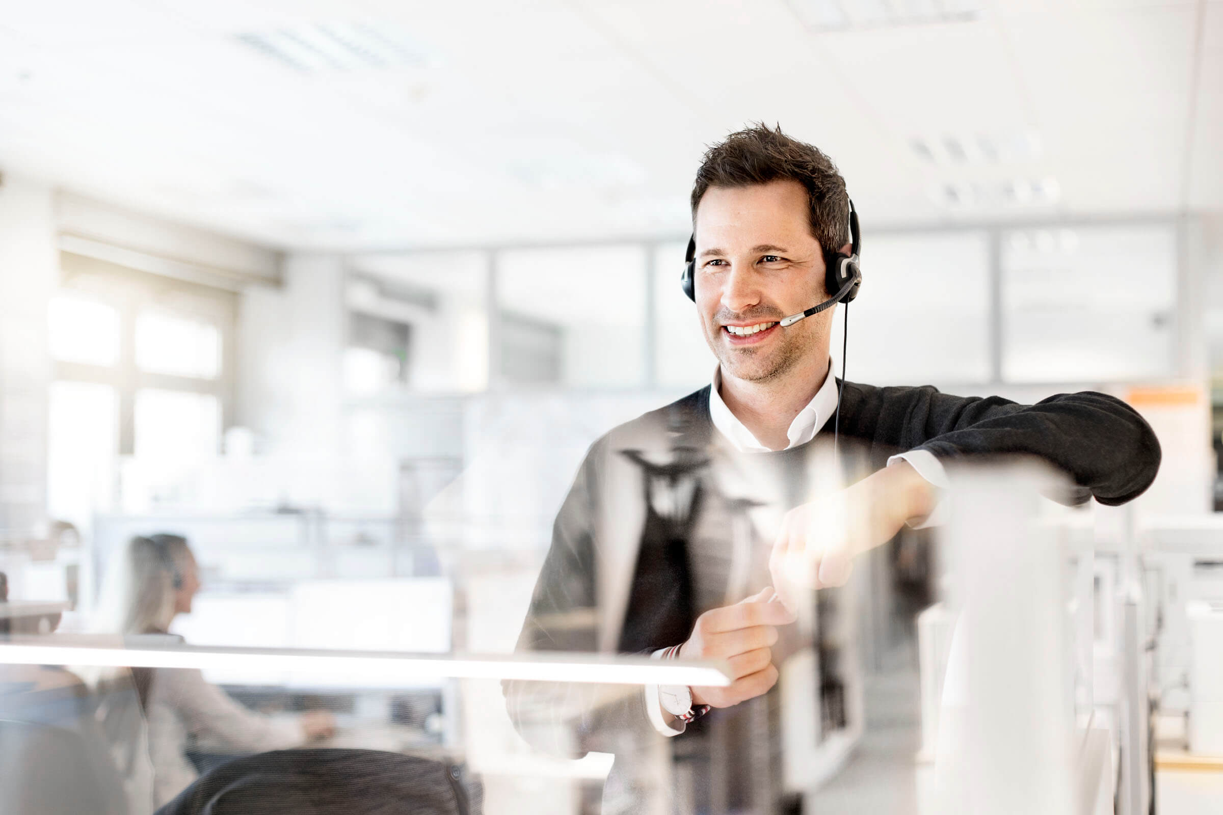 Ein Business Partners Mitarbeiter führt im Büro ein Kundengespräch über sein Headset.