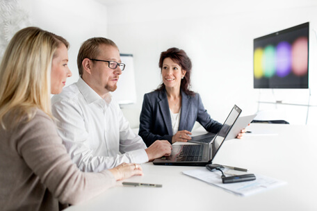 Drei comdirect Business Partners Mitarbeitende schauen in einem Büro gemeinsam auf einen Laptop-Bildschirm.