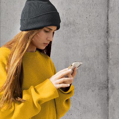 Eine junge Frau mit langen Haaren und Beanie-Mütze schaut konzentriert auf ihr Smartphone. Sie sucht nach Inspiration für ihr Depot und erhält dank der hi!stocks App Ideen und Impulse. 