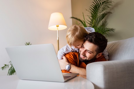 Ein Vater liegt mit seinem Kind auf einem Sofa am Laptop und freut sich über die Eröffnung eines Junior Depots für Kinder.