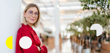 Eine junge Frau mit roter Bluse lehnt an einer Wand. Sie freut sich über hohe Zinsen für Aktienanleihen.