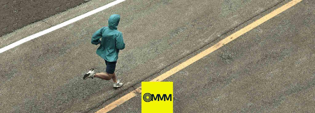 Ein Jogger mit grüner Jacke läuft eine Straße entlang.