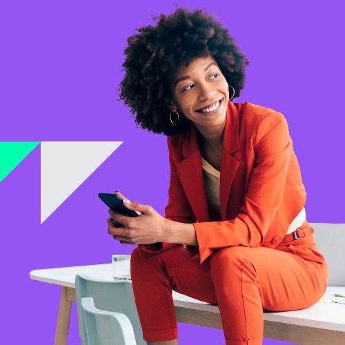 Eine junge Frau in einem Anzug sitzt l&auml;chelnd auf einem Tisch.