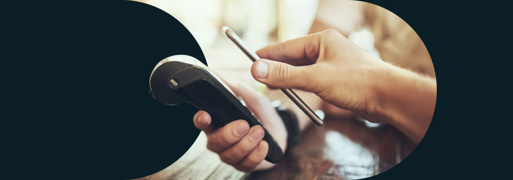 Eine Hand hält ein Smartphone zum mobilen Bezahlen mit Google Pay an ein Bezahl-Terminal.