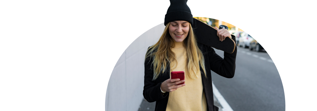 Eine junge Frau mit schwarzer Mütze und Skateboard auf der Schulter schaut auf ihr Smartphone. Sie nutzt den Google Assistant, um Aktienkurse abzufragen.