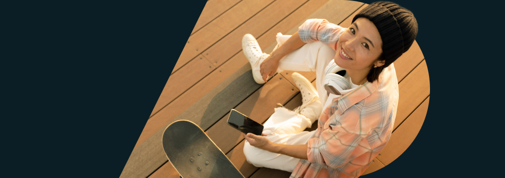 Eine junge Frau hält ein Handy, links neben ihr steht ein Skateboard.