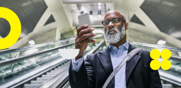 Ein bärtiger Mann mit Anzug und Brille fährt eine Rolltreppe hinunter und schaut dabei auf sein Smartphone.