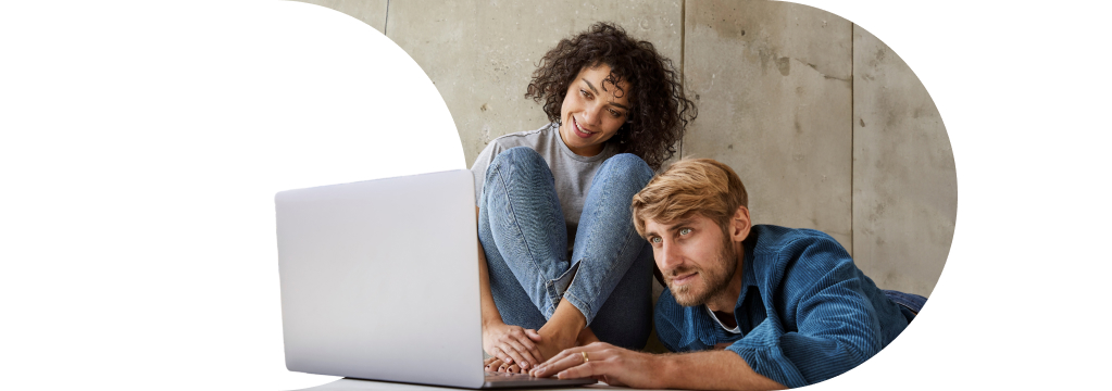 Eine junge, lockige Frau und ein blonder Mann sitzen gemeinsam auf dem Boden vor einem Laptop. Sie nutzen den PortfolioPlaner als Starthilfe für die Geldanlage.