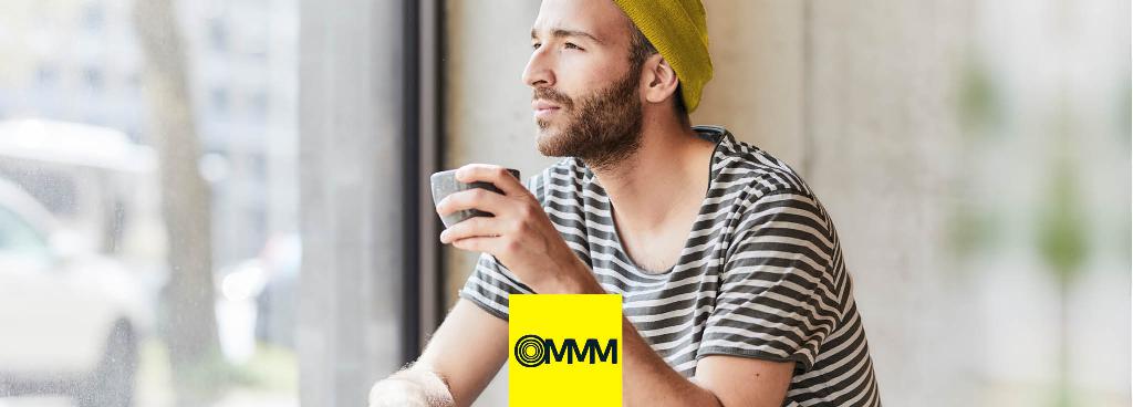 Ein junger Mann mit gelber Mütze sitzt mit seinem Kaffee an einem Fenster.