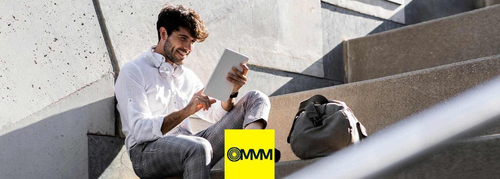 Ein junger Mann sitzt lachend auf einer Treppe und schaut auf sein weißes Tablet.