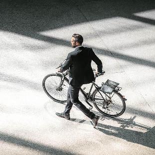 Ein Mann im Anzug schiebt eilig ein Fahrrad über eine große Fläche.