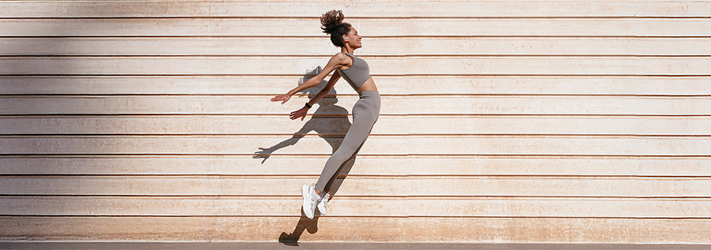 Frau springt voller Energie vor heller Wand