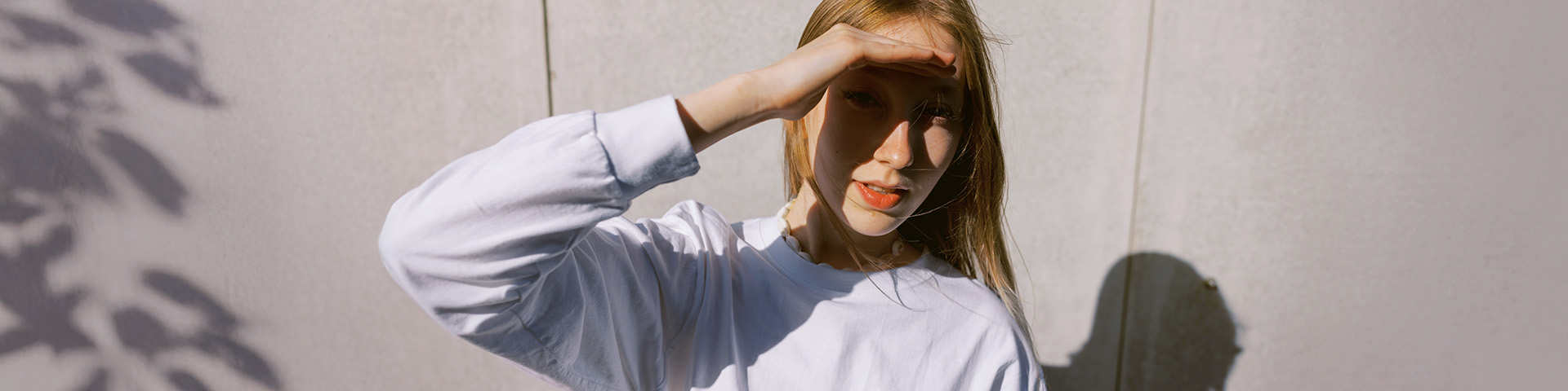 Junge Frau schaut suchend ins Licht und hebt die Hand