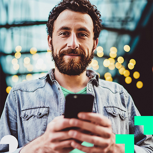 Mann mit Bart h&auml;lt ein Smartphone. Im Hintergrund sind Lichter zu sehen. Es gibt einen St&ouml;rer mit dem Text „Aktion“.