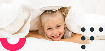 Ein blondes M&auml;dchen lugt unter einer wei&szlig;en Bettdecke hervor. Es st&uuml;tzt den Kopf auf die Arme und l&auml;chelt. Es befindet sich ein St&ouml;rer auf dem Bild mit dem Text „Bis 31.01.“