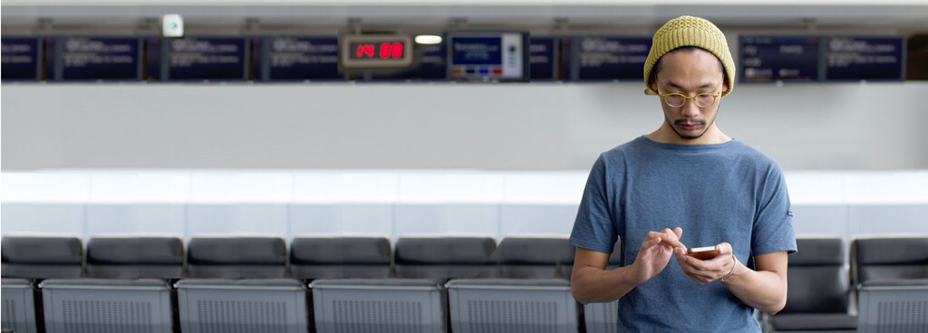 Ein junger Mann mit gelber Mütze und blauem T-Shirt führt auf seinem Smartphone eine Auslandsorder an internationalen Börsen durch.