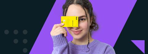 Eine junge Frau h&auml;lt eine Visa-Debitkarte vor ein Auge und l&auml;chelt in die Kamera.