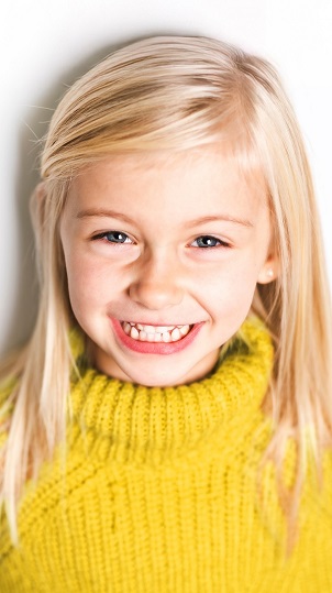 Ein blondes M&auml;dchen l&auml;chelt in die Kamera.