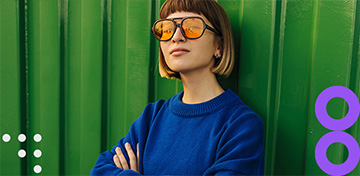 Eine junge Frau mit Sonnenbrille lehnt entspannt an einer Wand.