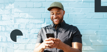 Ein junger Mann mit Basecap und Sommersprossen informiert sich gutgelaunt auf seinem Smartphone &uuml;ber Kryptohandel.