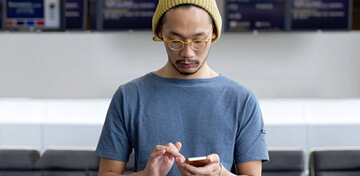 Ein junger Mann mit einer gelben Mütze und einem blauen T-Shirt schaut konzentriert auf sein Smartphone.